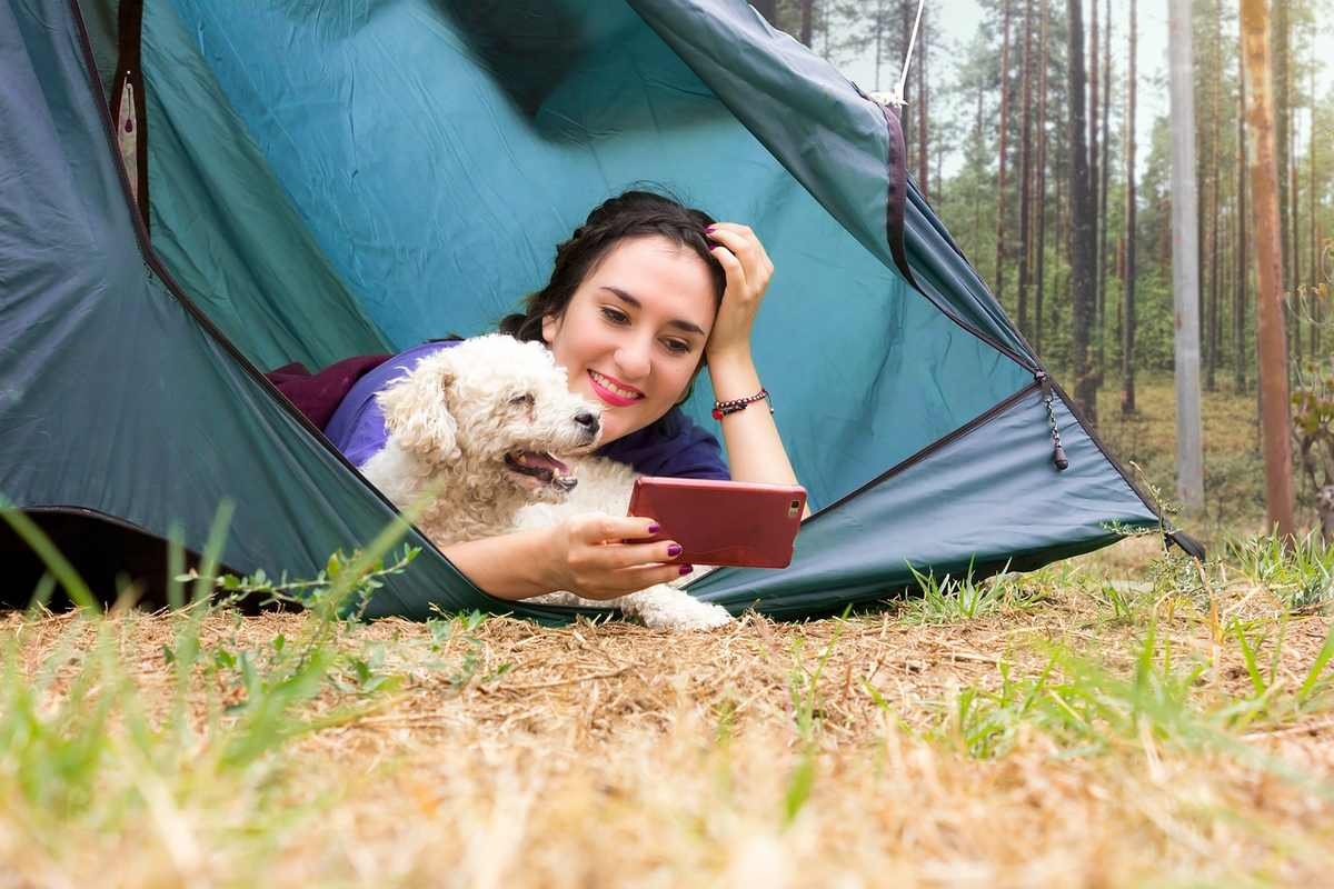 Femme allongée dans une tente bleue avec un petit chien beige, forêt en arrière-plan Femme allongée dans une tente bleue avec un petit chien beige, forêt en arrière-plan