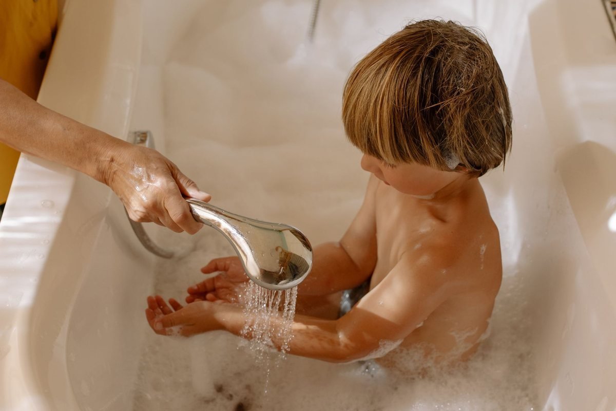 Un enfant se lave les mains sous l'eau d'un pommeau dans une baignoire Un enfant se lave les mains sous l'eau d'un pommeau dans une baignoire