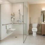 Salle de bain accessible senior, douche de plain-pied avec barre d'appui et siège, carrelage clair, lumineuse